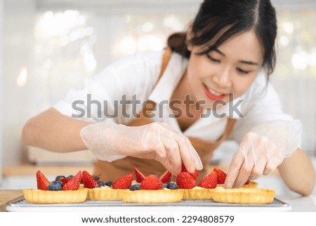 Young beautiful woman is baking in kitchen , bakery and coffee shop business. Hands in cooking gloves decorating freshly baked tart with blueberries strawberry fresh fruit. homemade bakery at home. Royalty-Free Stock Photo #2294808579