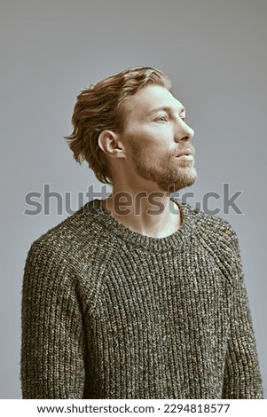 Art portrait of a handsome middle aged man with a curly haircut posing in a wide knitted sweater on a gray studio background. People, emotions. Male beauty and fashion. 
