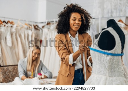 Multiracial female tailor is measuring chest circumference of a wedding dress on a doll Royalty-Free Stock Photo #2294829703