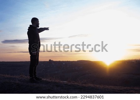 Man at sunset. He points his finger to the sky. Outstretched hand. Evening