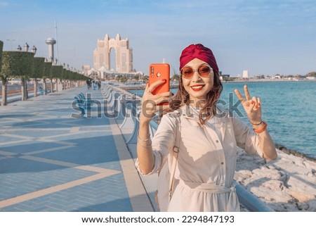 Embodying the spirit of modernity and progress in the UAE's capital city, a girl snaps a photo against the dazzling skyline of Abu Dhabi