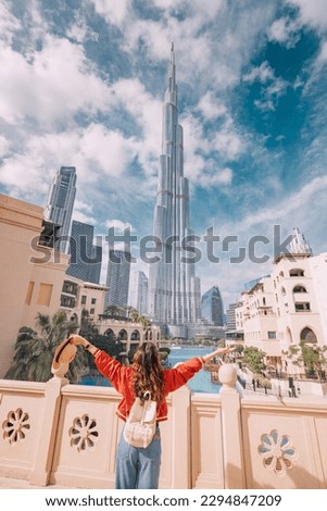 Happy girl arms are outstretched, as she embracing the incredible view before her with unreal Burj Khalifa tower in Dubai, UAE