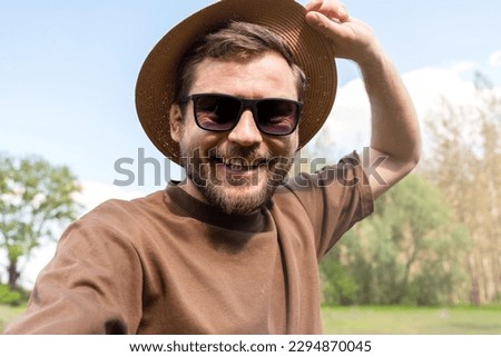Man wearing dark glasses and straw hat taking a selfie outdoors in summer, mental wellbeing and positive emotions concept. Royalty-Free Stock Photo #2294870045
