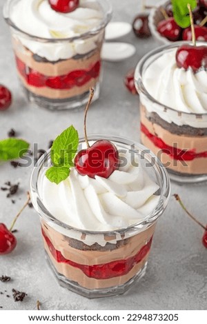 Dessert black forest cake in a glass. Chocolate trifle with chocolate cream, biscuit and cherry on a gray concrete background