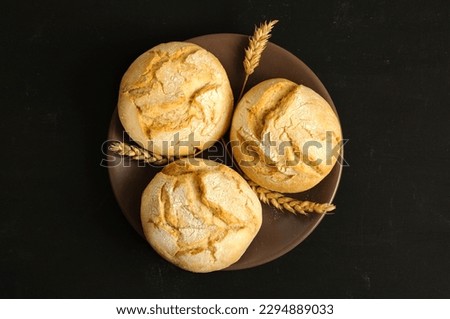 Freshly baked round buns on a brown plate. Black background, top view, natural light, selective focus