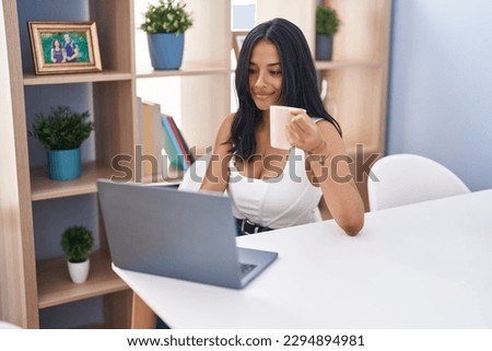 Young hispanic woman using laptop drinking coffee at home