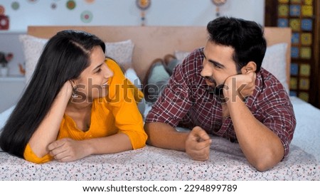 Smiling couple in casual clothes talking while laying down in bed - Young Indian couple, Newly married couple, Indian family. Young Indian husband-wife spending time together while relaxing at home... Royalty-Free Stock Photo #2294899789