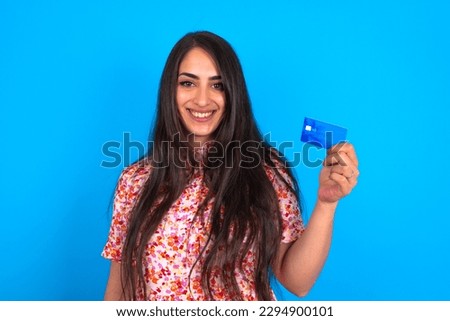 Photo of happy cheerful smiling positive beautiful brunette woman wearing floral dress over blue background recommend credit card