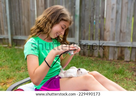 Kid girl taking photos to puppy dog pet with camera in outdoor backyard