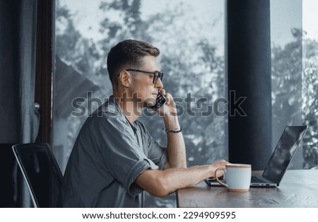 Handsome man call in smartphone, happy face, outdoor hipster portrait on the cafe, smile happy face, listen music on headphones, text, messenger, hipster, player,photo concept, laptop, coffee cup