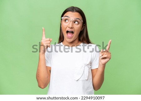 Young caucasian woman isolated on green chroma background surprised and pointing up