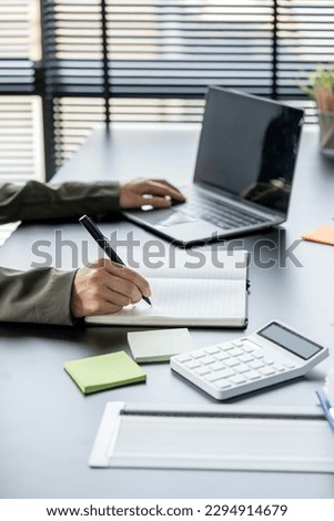 Businesswoman hand writing note or business plan and working on laptop computer at her desk in modern office.