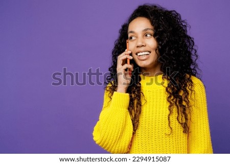 Young woman of African American ethnicity wear casual yellow sweater doing selfie shot on mobile cell phone post photo on social network isolated on plain purple background studio. Lifestyle concept