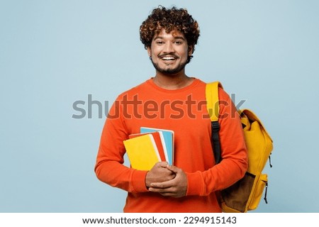 Young smiling happy fun cheerful teen Indian boy student he wearing casual clothes backpack bag hold books isolated on plain pastel light blue cyan background. High school university college concept