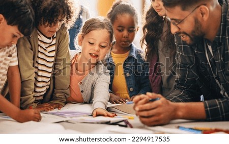 Students doing a creativity project with their teacher in a classroom. Group of primary school children learning how to draw and colour with the help of their educator. Royalty-Free Stock Photo #2294917535
