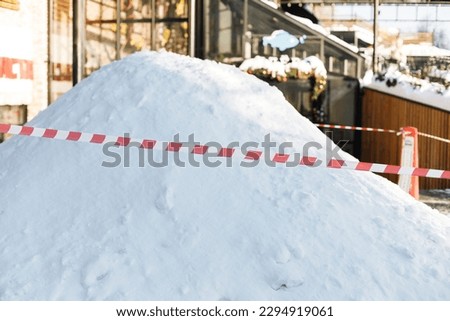 A big snowdrift, a pile of uncollected snow. Striped red and white signal tape encloses a place for cleaning on the street. Municipal service in the city. Moscow, Russia. Royalty-Free Stock Photo #2294919061