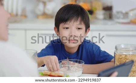 Cute little boy watching cartoons on tablet sitting in cozy kitchen at home. Little boy eating cereals for breakfast and watching a tablet in a kitchen