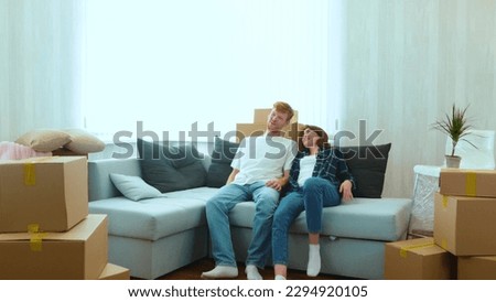 Cheerful Caucasian couple boyfriend and girlfriend moving in together in new house in good mood. Tired happy young married couple sitting down on sofa in new home with many boxes on moving day Royalty-Free Stock Photo #2294920105