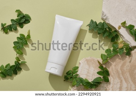 A white tube displayed with some stones and green leaves. Mockup of skin care cosmetic tube of beauty facial. Top view