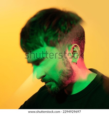 Artistic creative portrait through prism. Man looking down in green, pink neon lights on yellow background. Modern photo handsome bearded middle age man with earring in the ear. Kaleidoscopic effect.