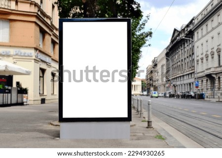 white blank advertising billboard. street mockup panel. digital lightbox poster ad banner board. bus shelter advertising. green park background. vertical format sign. stucco facades. european scene