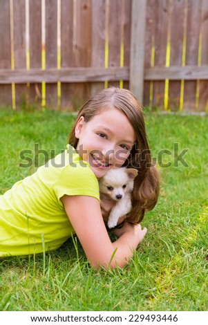 kid girl and puppy dog happy playing with chihuahua pet lying in backyard lawn
