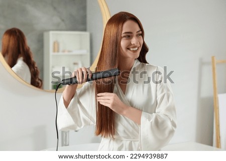 Beautiful woman using hair iron in room Royalty-Free Stock Photo #2294939887