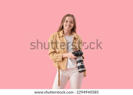 Young female photographer with professional camera on pink background