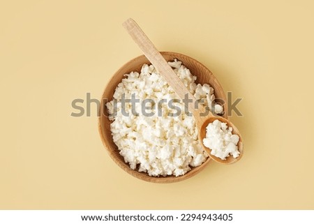 Bowl and spoon with tasty cottage cheese on yellow background Royalty-Free Stock Photo #2294943405