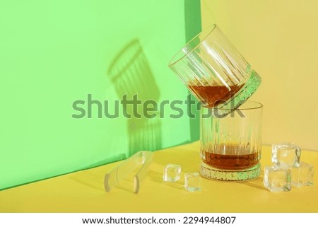 Glasses of rum with ice cubes and tongs on green background