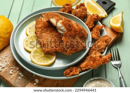 Plates of tasty fried codfish with lemon on green wooden background
