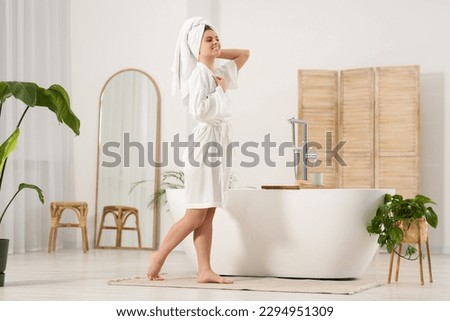 Beautiful happy woman wearing white robe near tub in bathroom Royalty-Free Stock Photo #2294951309