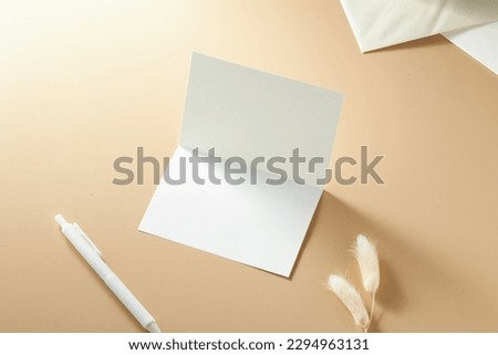 Mock up of a Blank white paper greeting card on a cream-colored background and stationary object surrounding it.