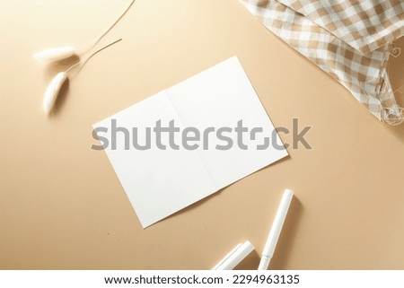 Mock up of a Blank white paper greeting card on a cream-colored background and stationary object surrounding it.