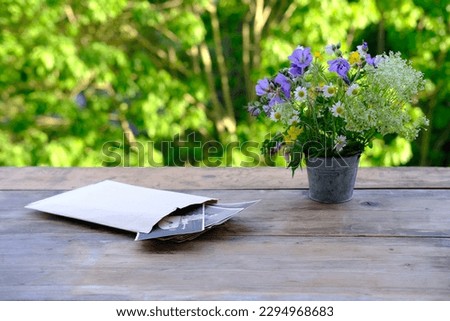 paper envelope with old vintage photographs, bouquet of wild flowers on table wooden table in garden, blurred natural background, green foliage, concept of genealogy, memory of ancestors, family tree