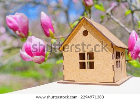 Tiny wooden house model set against a pink magnolia flowers in full bloom. Renewal and new beginnings of the season.