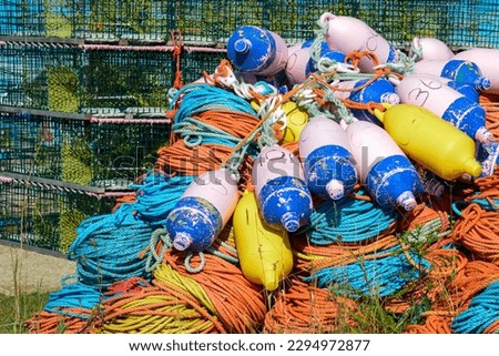 Bundles of commercial nylon woven fishing line orange, yellow, blue, and green color. There are multiple pink buoys piled on top of the rope. The fishing gear is in a pile on a concrete platform.  Royalty-Free Stock Photo #2294972877