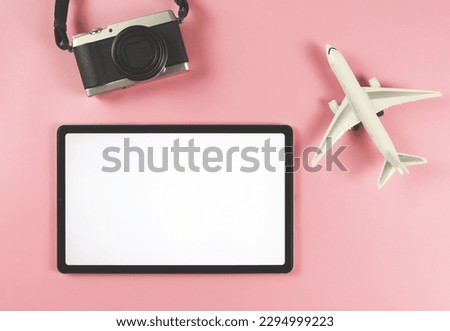 Top view or flat lay of digital tablet with blank white screen, airplane model and digital camera isolated on pink background. travel planning concept.