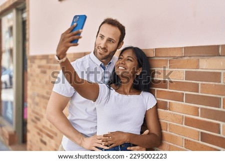 Man and woman interracial couple making selfie by smartphone at street