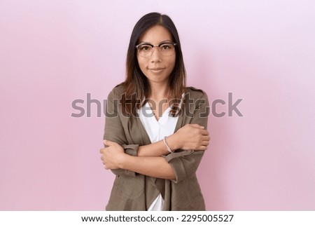 Middle age chinese woman wearing glasses over pink background happy face smiling with crossed arms looking at the camera. positive person. 