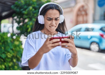 Young beautiful hispanic woman playing video game at street