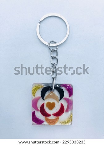 This key tag is square shape on a white background.The inside of the key tag has half circle shapes with yellow, pink, black, red, orange colours. also the inside of the keytag has small orange heart.