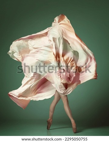 Young woman, ballerina dancing with elegance movements and fabric cover the face over dark green studio background. Ballet with silk dress. Concept of classical dance, inspiration, motion, creativity