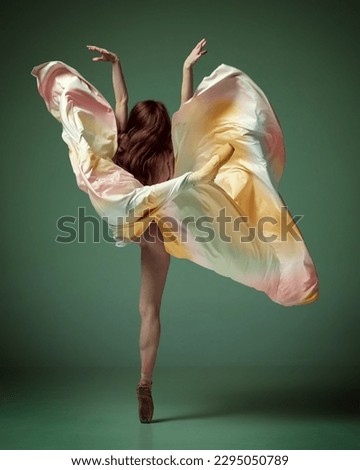 Aesthetic of movement. Back view of one charming ballerina, ballet dancer wearing fancy colorful dress posing on tiptoe over dark green studio background. Concept of inspiration, dance, creativity