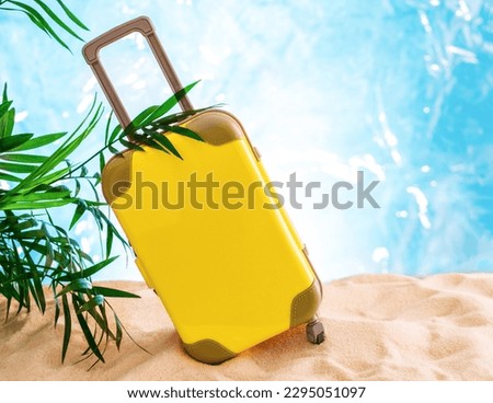 Vertical stock photo of yellow suitcase on a sandy beach with palm leaves. Summer travel advertising concept. Copy space.
