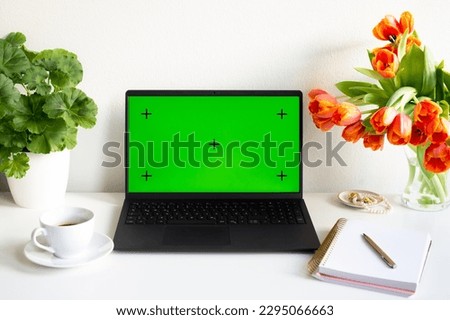 Mock-up scene with a green screen for Mother's day with orange tulips and a black laptop on a white desk
