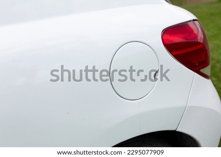 Detail of a white gas cap on a silver metallic car. Red tail light of a white car.