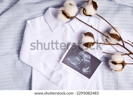 new born baby infant clothes,white bodysuit and booties knitted pattern on blanket with cotton dry branch.word baby and it's a boy.safe organic textile.ultrasound picture of fetus over clothes. blue