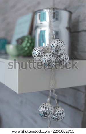 Silver balls on a string as decoration on a white book shelf mounted on the wall 