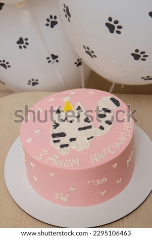 pink cake with a picture of a cat in a hat, balloons, the inscription on the cake "Happy Birthday"